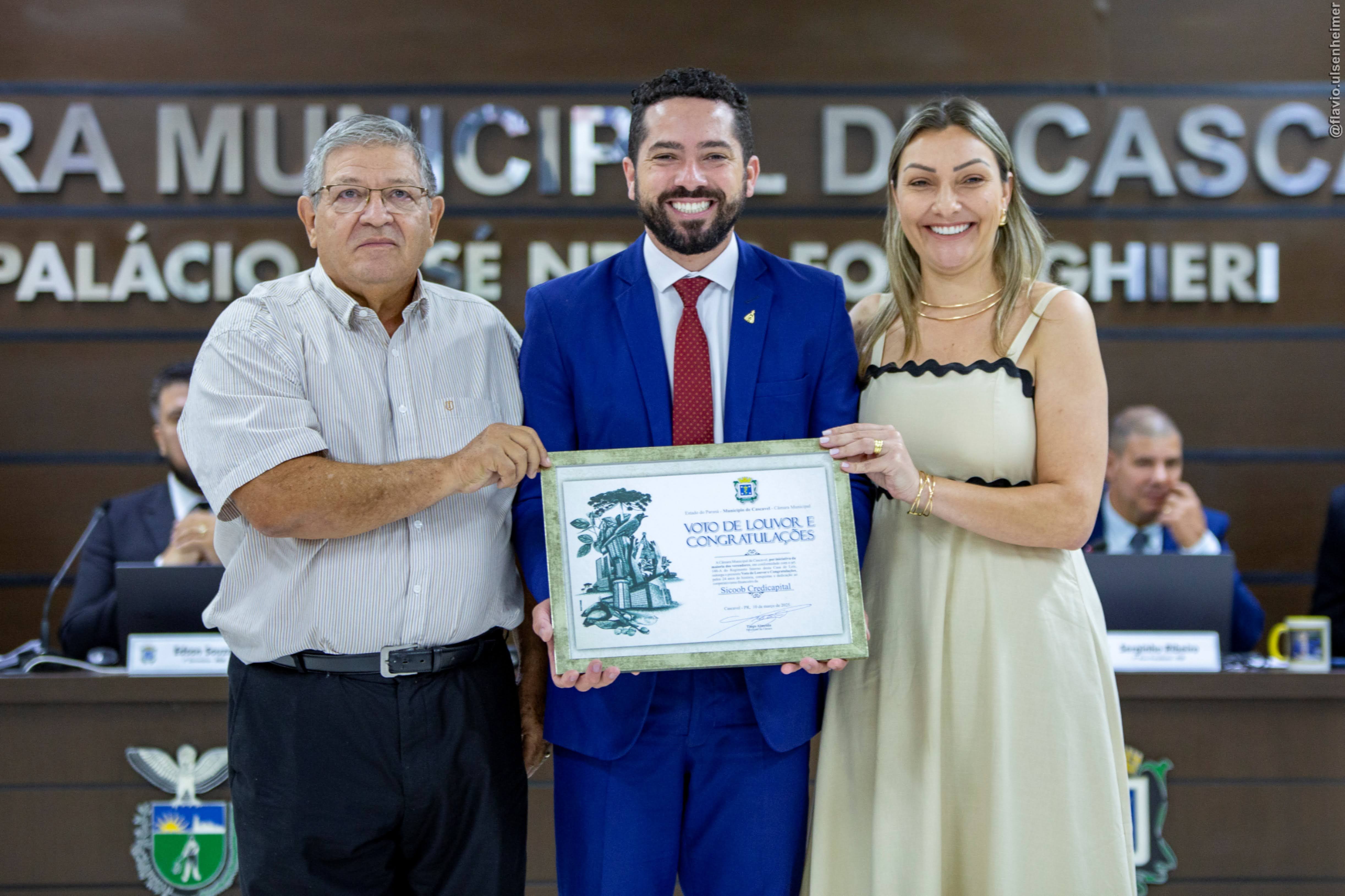 Tiago Almeida (centro) entrega homenagem a João Irani Flores (esq.) e Manuela Santolin (dir.)