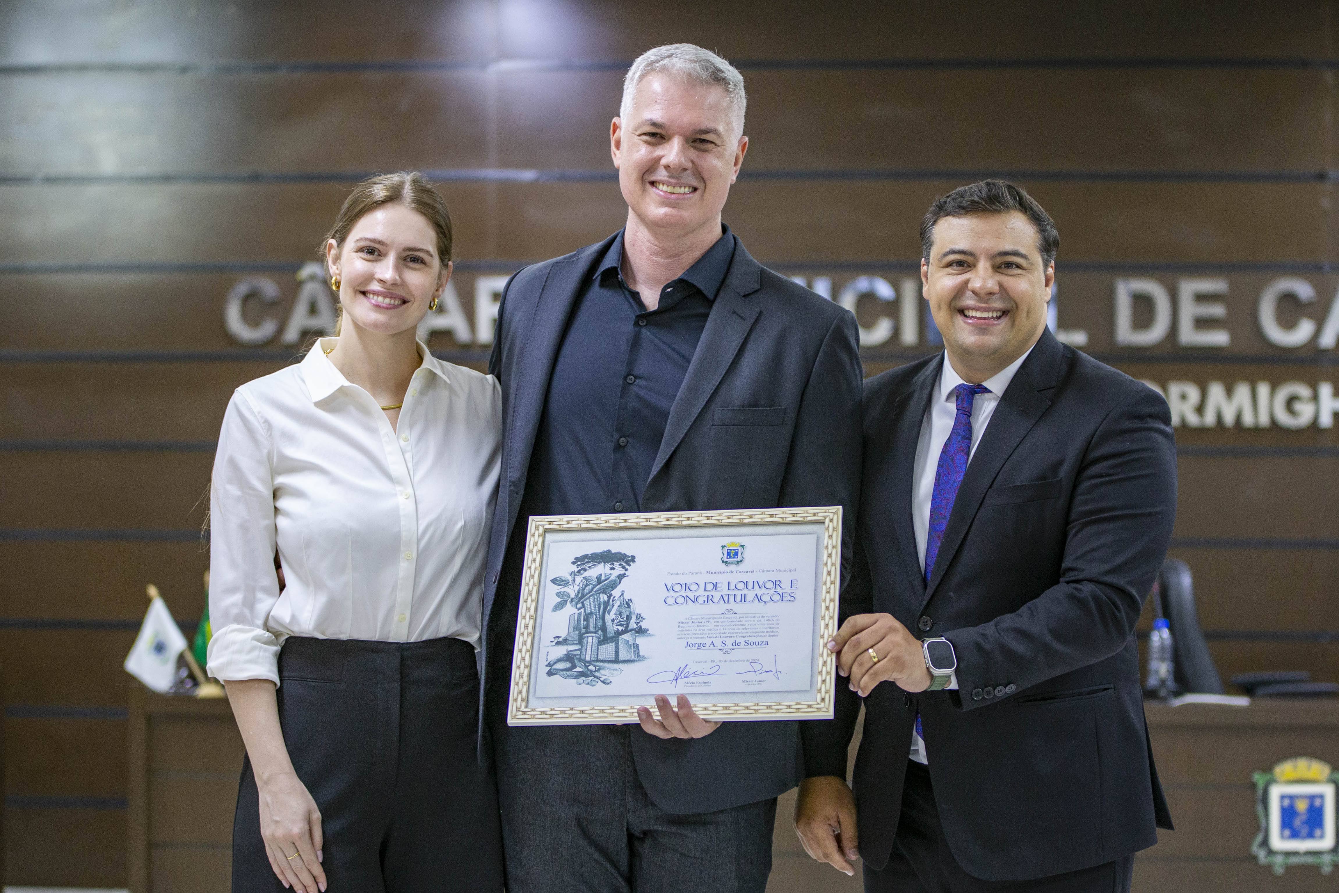 Ao lado da esposa, dr.Jorge (centro) recebe homenagem das mãos do vereador Misael Junior